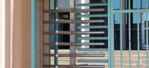 Rustic turquoise turnstile and gate entrance to a building, bathed in natural light.