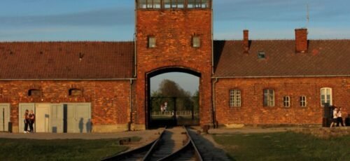View of the iconic Auschwitz-Birkenau entrance gate at sunset in Oświęcim, Poland.